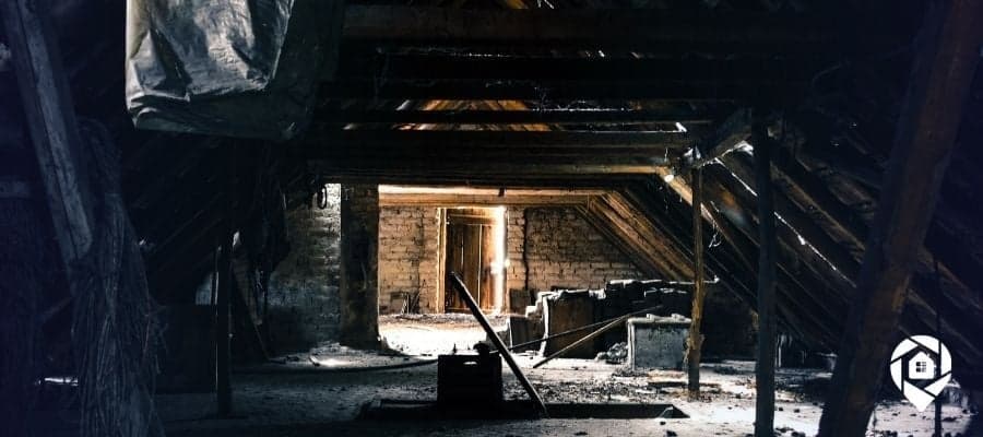 Abandoned attic with wooden beams and light shining through a doorway.