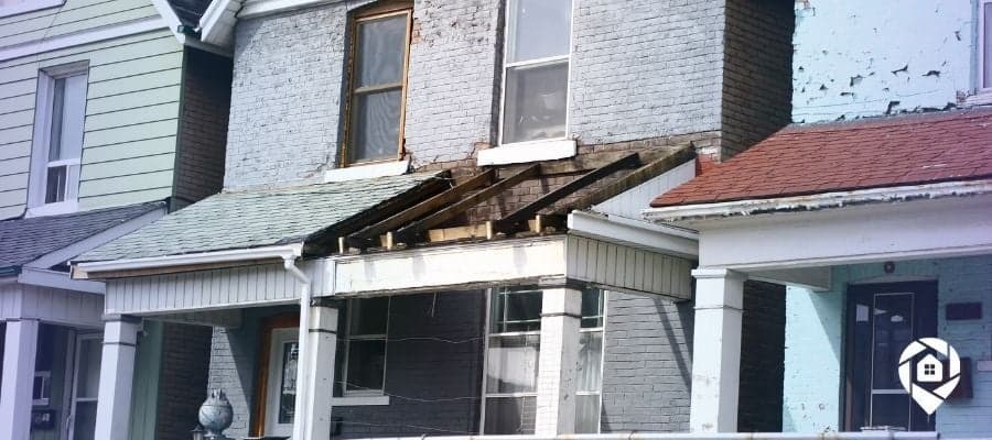 Distressed two-story house with damaged porch—ideal for real estate flipping and investment.
